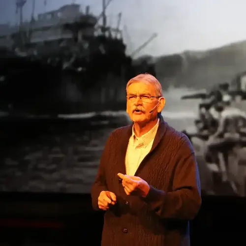 man speaking with warship image behind him